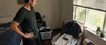 Man in a bedroom picking a polo shirt, chinos, and clean sneakers laid out as a golf-style summer outfit on a chair